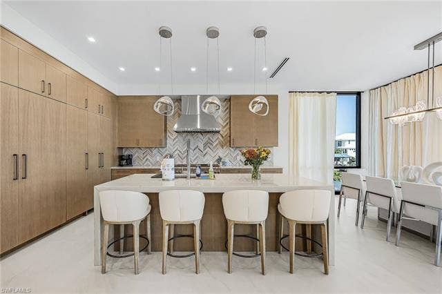 455 Palermo Cir, Fort Myers Beach, FL 33931 Kitchen with hanging light fixtures, a kitchen bar, light stone countertops, backsplash, and a center island with sink - Virtually Edited Image
