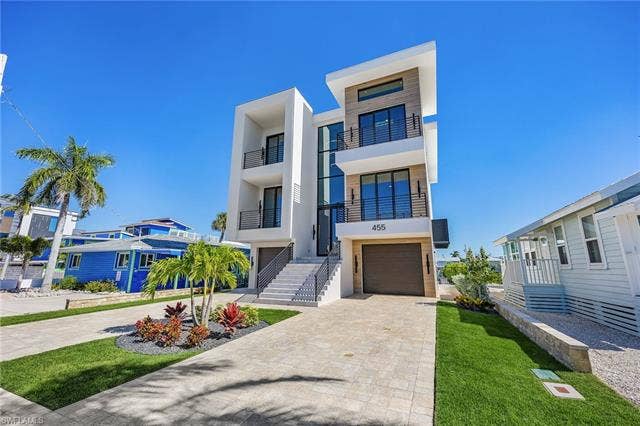 455 Palermo Cir, Fort Myers Beach, FL 33931 Modern home with decorative driveway, stucco siding, an attached garage, a balcony, and a front lawn - Virtually Edited Image