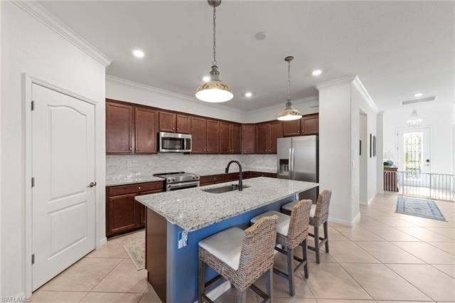 19712 The Place Blvd, Estero, FL 33928 Kitchen featuring wood cabinetry, stainless steel appliances, a center island with a light-toned countertop, and tile flooring