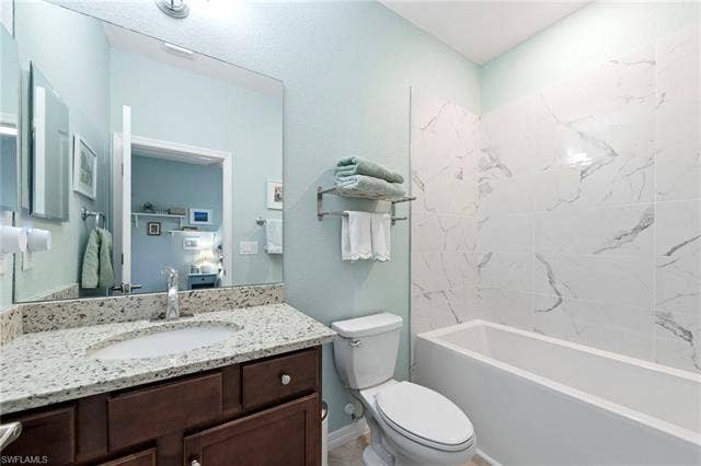 19712 The Place Blvd, Estero, FL 33928 Upgraded soaker tub with white tile surround, dark wood-finish vanity with stone countertop, and an integrated sink with a chrome faucet