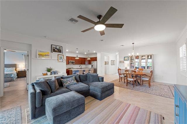 19712 The Place Blvd, Estero, FL 33928 Open-concept living area featuring light-toned tile flooring, a dining area with a chandelier, and a kitchen with warm wood-finish cabinetry