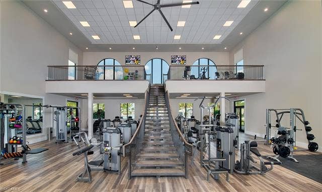 19712 The Place Blvd, Estero, FL 33928 High-ceiling fitness area featuring wood-finish flooring, a grand staircase with metal railings, and a second-story fitness loft with arched windows