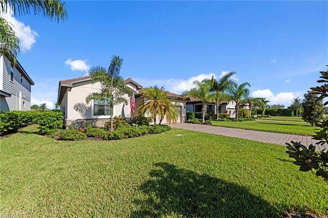 19712 The Place Blvd, Estero, FL 33928 Stucco exterior with stone veneer accents, tile roof, lush landscaping featuring palm trees, and a paver driveway