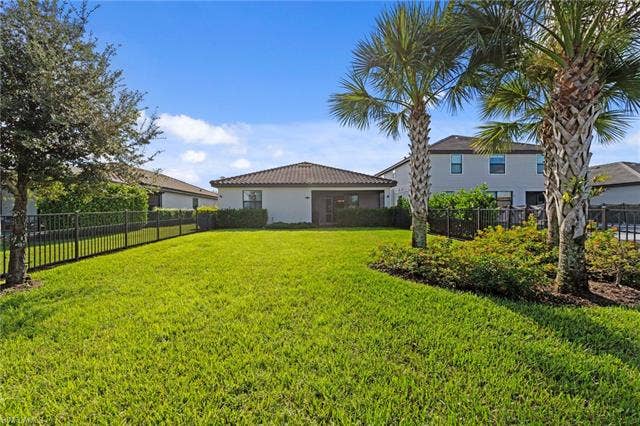 19712 The Place Blvd, Estero, FL 33928 Expansive fenced backyard featuring a manicured lawn, mature palm trees, and established landscaping. Room for a pool and great for pets or children.