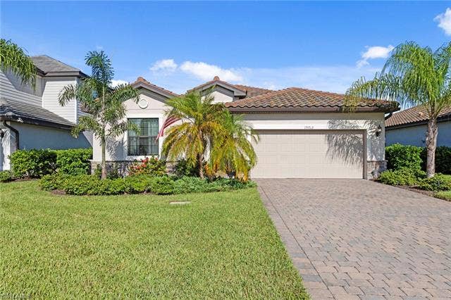 19712 The Place Blvd, Estero, FL 33928 Mediterranean-style exterior featuring a tile roof, paver driveway, attached garage, and mature landscaping