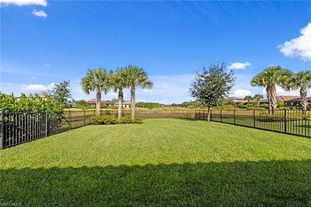 19712 The Place Blvd, Estero, FL 33928 Expansive green lawn with a black metal fence, bordered by mature palm trees and lush landscaping. Plenty of room for a pool. Great area for pets or children.