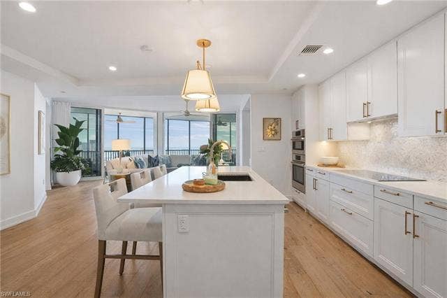 4142 Bay Beach Ln, #904, Fort Myers Beach, FL 33931 Kitchen featuring white cabinetry, open floor plan, pendant lighting, a center island with sink, and a breakfast bar area - Virtually Edited Image