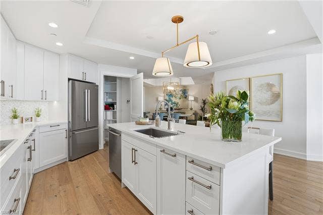 4142 Bay Beach Ln, #904, Fort Myers Beach, FL 33931 Kitchen with white cabinets, decorative light fixtures, appliances with stainless steel finishes, light wood-type flooring, and a kitchen island with sink - Virtually Edited Image