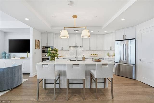 4142 Bay Beach Ln, #904, Fort Myers Beach, FL 33931 Kitchen with appliances with stainless steel finishes, white cabinets, a kitchen bar, hanging light fixtures, and an island with sink - Virtually Edited Image