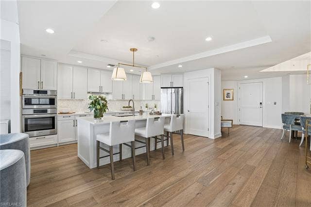 4142 Bay Beach Ln, #904, Fort Myers Beach, FL 33931 Kitchen with a raised ceiling, a breakfast bar, pendant lighting, a center island with sink, and white cabinetry - Virtually Edited Image