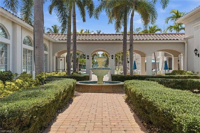 20052 Serene Meadow Ln, Estero, FL 33928 Brick paver pathway with manicured hedges, centered water feature, and arched architectural details