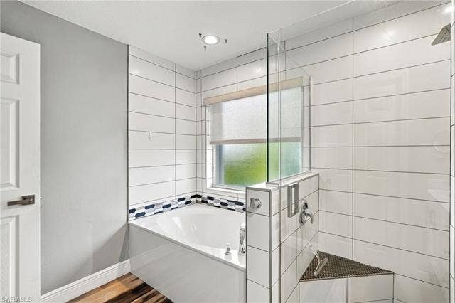 20052 Serene Meadow Ln, Estero, FL 33928 Built-in soaking tub with decorative tile accents, glass-enclosed shower with a built-in bench, and wood-finish flooring