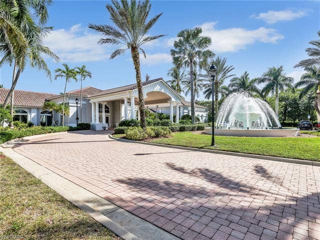 20052 Serene Meadow Ln, Estero, FL 33928 Clubhouse entrance featuring a porte-cochère, columned façade, tile roof, extensive paver driveway, and a central water fountain feature