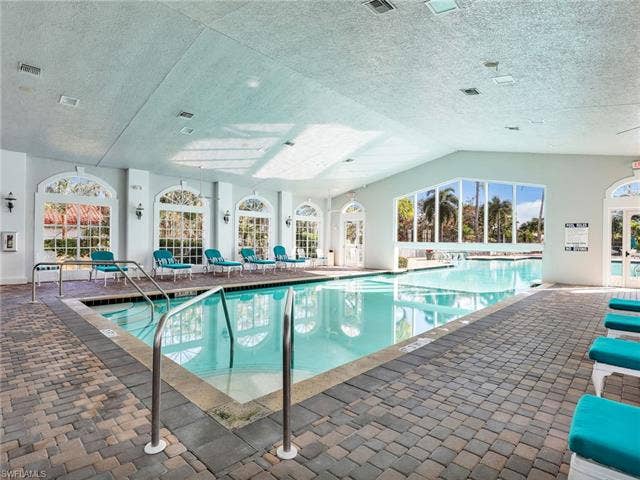 20052 Serene Meadow Ln, Estero, FL 33928 Indoor pool with paver decking, arched windows, and a vaulted ceiling