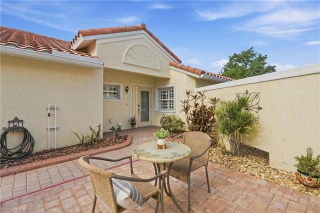 20052 Serene Meadow Ln, Estero, FL 33928 Tiled roofline, stucco exterior, paver patio, privacy wall, and mature landscaping