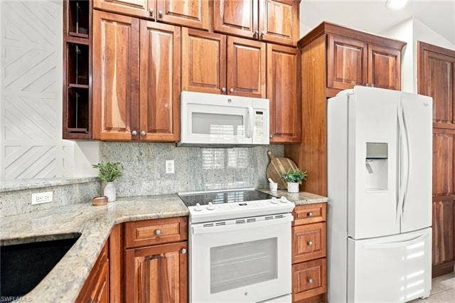20052 Serene Meadow Ln, Estero, FL 33928 White appliances, wood-finish cabinetry, light-toned countertops, and a tile backsplash