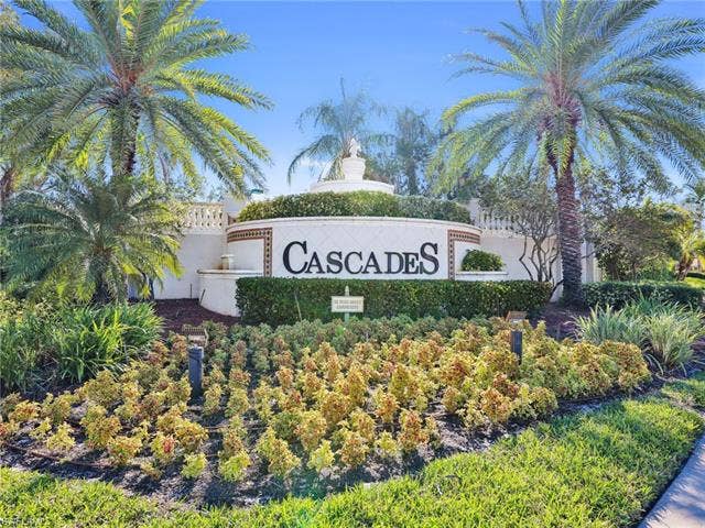 20052 Serene Meadow Ln, Estero, FL 33928 Cascades community entrance featuring a tiered fountain, decorative wall with tile accents, mature palm trees, and lush landscaping