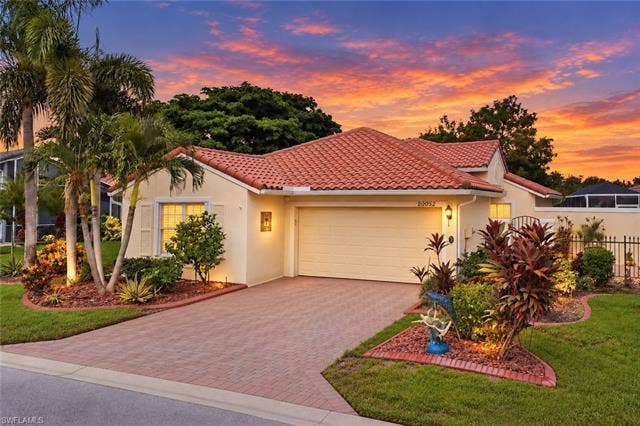 20052 Serene Meadow Ln, Estero, FL 33928 Mediterranean-style residence featuring a terracotta tile roof, paver driveway, and a two-car garage