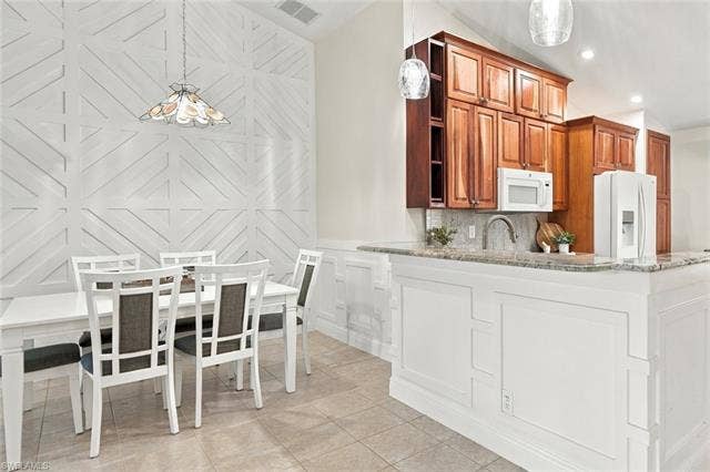 20052 Serene Meadow Ln, Estero, FL 33928 Vaulted ceiling with decorative wall paneling, built-in kitchen cabinetry, and a granite-topped peninsula