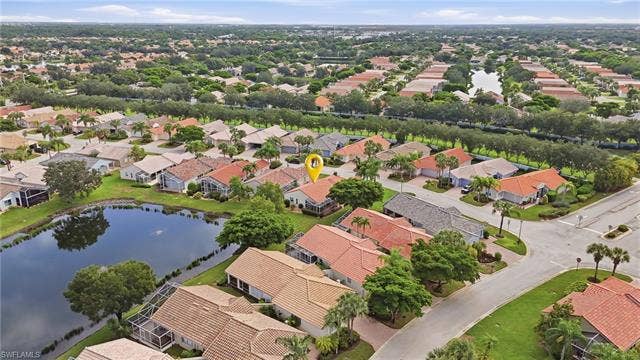 20052 Serene Meadow Ln, Estero, FL 33928 Lakeside property featuring a red tile roof, screened lanai, and mature landscaping within a residential community