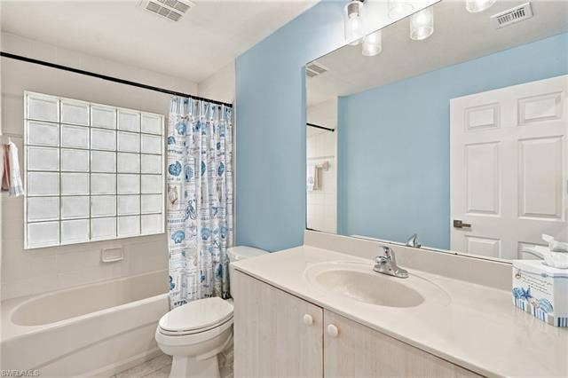 20052 Serene Meadow Ln, Estero, FL 33928 Bathtub with glass block window, single vanity with integrated sink, and large wall-mounted mirror