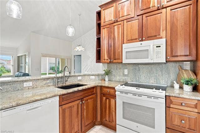 20052 Serene Meadow Ln, Estero, FL 33928 Kitchen featuring abundant wood-finish cabinetry, light-toned granite countertops, and a full suite of white appliances