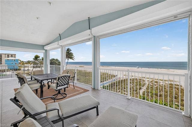 61 Mango St, Fort Myers Beach, FL 33931 Expansive enclosed balcony with a vaulted ceiling, concrete flooring, and direct beach frontage - Virtually Edited Image