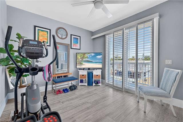 61 Mango St, Fort Myers Beach, FL 33931 Wood-finish flooring, ceiling fan, sliding glass doors with louvered shutters, and a balcony with metal railings - Virtually Edited Image
