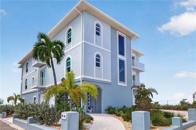 61 Mango St, Fort Myers Beach, FL 33931 Multi-story exterior with light blue stucco facade, arched windows, and multiple balconies - Virtually Edited Image