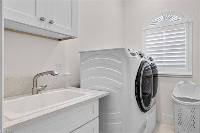 61 Mango St, Fort Myers Beach, FL 33931 Laundry room featuring shaker-style upper cabinetry, a utility sink with a brushed nickel faucet, a stone-finish countertop, and an arched window with plantation shutters - Virtually Edited Image