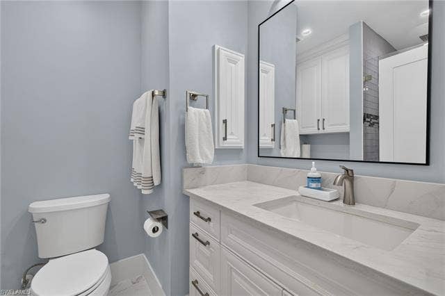 61 Mango St, Fort Myers Beach, FL 33931 White vanity with recessed panel cabinet doors, an integrated rectangular sink, a stone-finish countertop, and a black-framed mirror - Virtually Edited Image