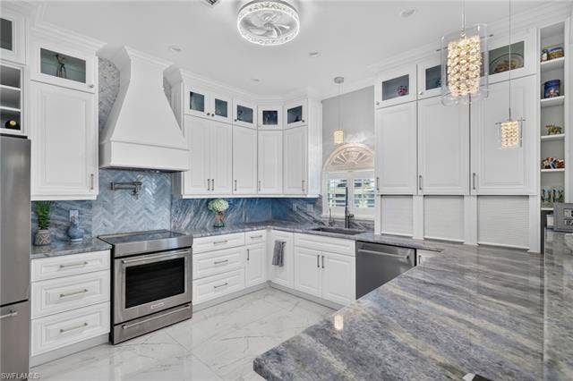 61 Mango St, Fort Myers Beach, FL 33931 White cabinetry, stainless steel appliances, patterned tile backsplash, polished stone countertops, and built-in shelving - Virtually Edited Image