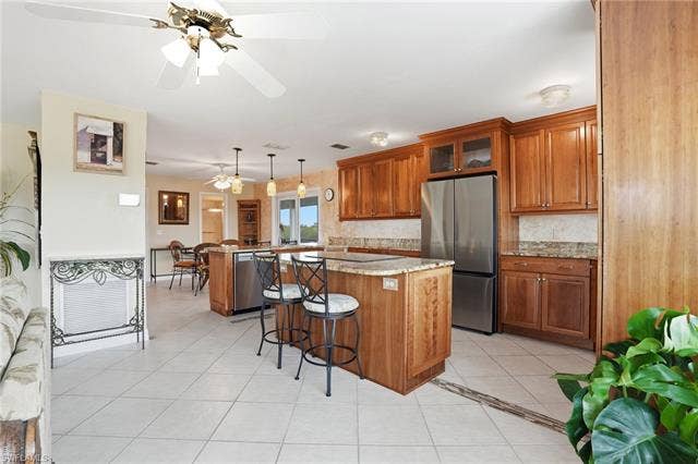 48 Fairview Blvd, Fort Myers Beach, FL 33931 Kitchen with brown cabinetry, appliances with stainless steel finishes, a kitchen island, and light tile patterned floors - Virtually Edited Image