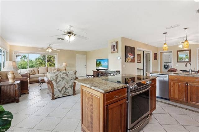 48 Fairview Blvd, Fort Myers Beach, FL 33931 Kitchen featuring a ceiling fan, light stone counters, brown cabinetry, appliances with stainless steel finishes, and hanging light fixtures - Virtually Edited Image