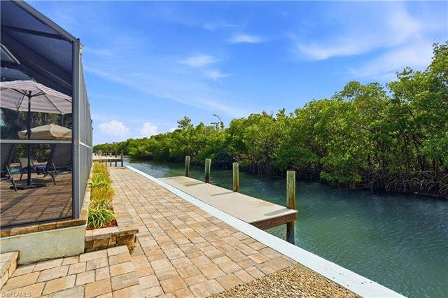 48 Fairview Blvd, Fort Myers Beach, FL 33931 Dock area with glass enclosure, a water view, a patio, view of scattered trees, and a sunroom - Virtually Edited Image