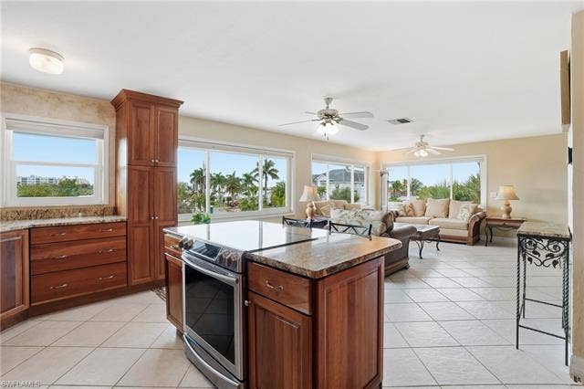48 Fairview Blvd, Fort Myers Beach, FL 33931 Kitchen with stainless steel range with electric cooktop, light tile patterned flooring, brown cabinetry, dark stone counters, and a center island - Virtually Edited Image