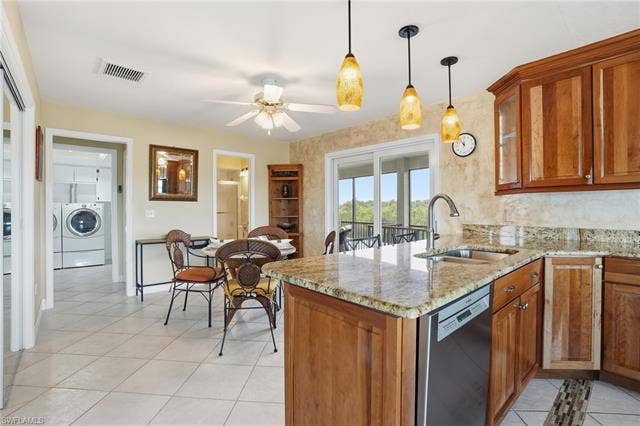 48 Fairview Blvd, Fort Myers Beach, FL 33931 Kitchen with brown cabinetry, light stone counters, pendant lighting, dishwasher, and a peninsula - Virtually Edited Image