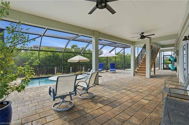 48 Fairview Blvd, Fort Myers Beach, FL 33931 View of patio / terrace featuring stairway, ceiling fan, glass enclosure, and a sunroom - Virtually Edited Image