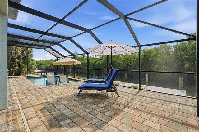 48 Fairview Blvd, Fort Myers Beach, FL 33931 View of patio / terrace with glass enclosure, an outdoor pool, and a sunroom - Virtually Edited Image