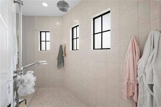 9796 Strike Ln, Bonita Springs, FL 34135 Tiled shower with a rainfall showerhead, handheld shower fixture, and three frosted windows with black grilles
