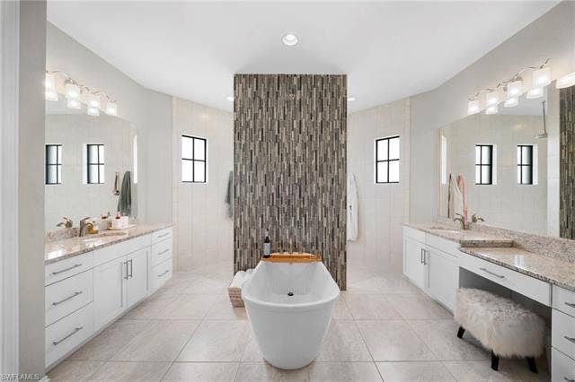 9796 Strike Ln, Bonita Springs, FL 34135 Freestanding soaking tub with a tiled accent wall, dual vanity areas with granite countertops, and light-toned floor tiling