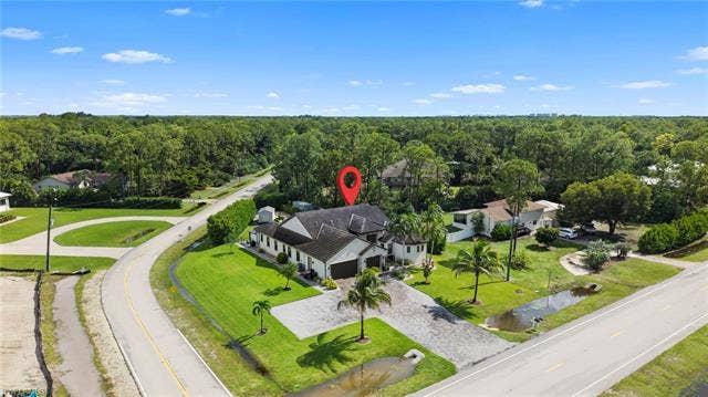 9796 Strike Ln, Bonita Springs, FL 34135 Expansive property featuring lush green lawns, mature palm trees, and a substantial driveway with a two-car garage