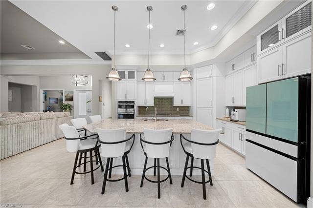 9796 Strike Ln, Bonita Springs, FL 34135 Gourmet kitchen featuring a large central island with seating, pendant lighting, white cabinetry, a built-in oven, and tile flooring