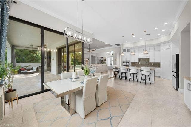 9796 Strike Ln, Bonita Springs, FL 34135 Expansive tile flooring throughout, featuring a modern kitchen with white cabinetry and stainless steel appliances, a breakfast bar with pendant lighting, and a dining area with a contemporary chandelier