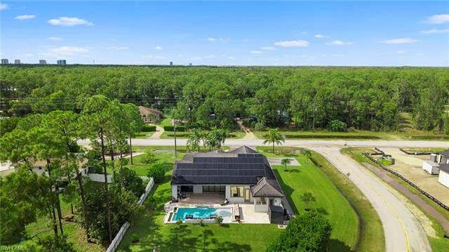 9796 Strike Ln, Bonita Springs, FL 34135 Single-story residence featuring a private pool, an expansive paved patio, lush green landscaping, a white privacy fence, and a solar panel system