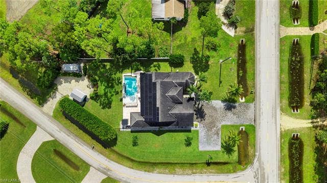 9796 Strike Ln, Bonita Springs, FL 34135 Property featuring a swimming pool with surrounding patio, a dark-toned roof with solar panels, a gravel driveway, and mature landscaping