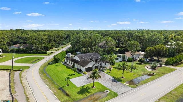 9796 Strike Ln, Bonita Springs, FL 34135 Expansive property featuring a large residence with a multi-car garage, extensive paved driveway, and mature palm trees