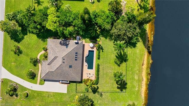 1936 Empress Ct, Naples, FL 34110 Expansive almost 1 Acre lot property featuring a private swimming pool, fenced backyard, concrete patio, lush green lawn, mature trees, and direct water frontage