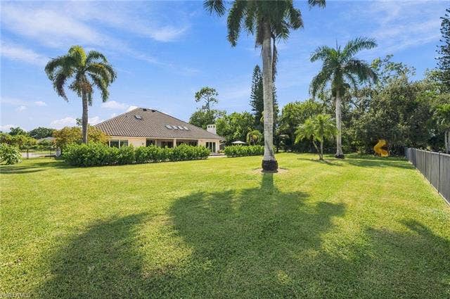 1936 Empress Ct, Naples, FL 34110 Expansive backyard green lawn with mature palm trees and established perimeter landscaping, offering a stucco exterior and a tile roof