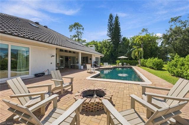 1936 Empress Ct, Naples, FL 34110 Brick paver patio with a built-in fire pit, dark-hued swimming pool, and extensive landscaping